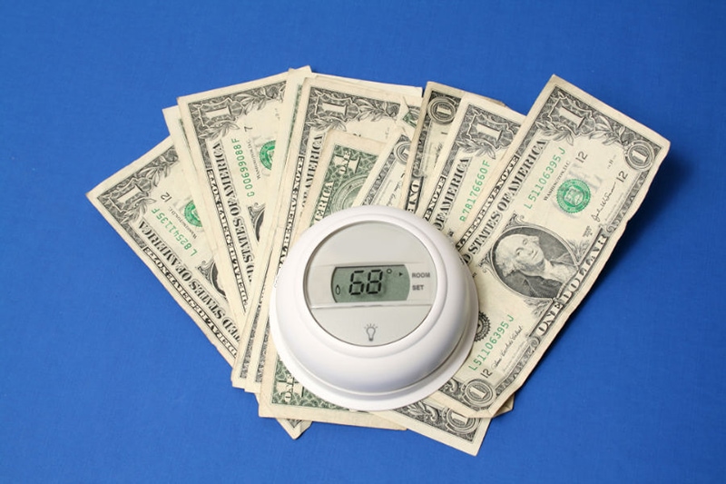 Thermostat on dollar bills on blue background.