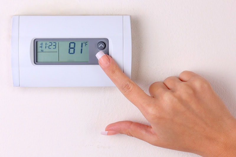 Thermostat 101 Basics. A woman changing the temperature on the thermostat.