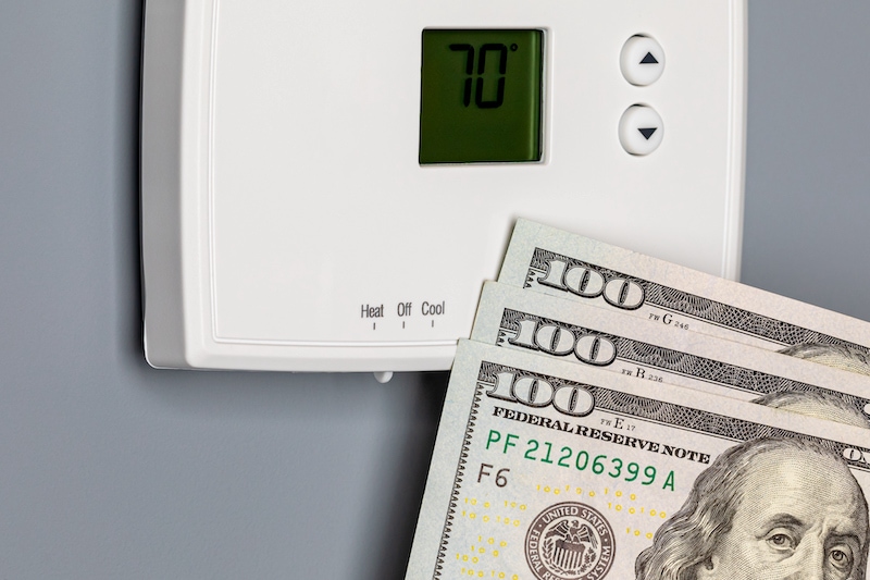 2024 HVAC Tax Incentives. Image is a photograph of a thermostat with 3 one hundred dollar bills stacked in front of the bottom right corner.