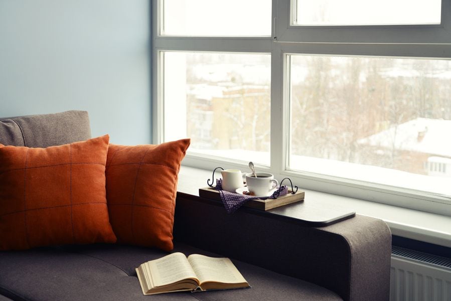 Why Is the Furnace Pilot Light Going Out? Image shows an open book and tea set on couch beside a window looking out at snow.